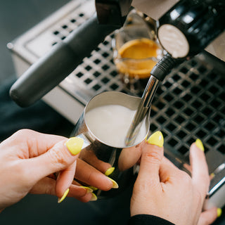 Hands steaming milk with a steam wand on an espresso machine.